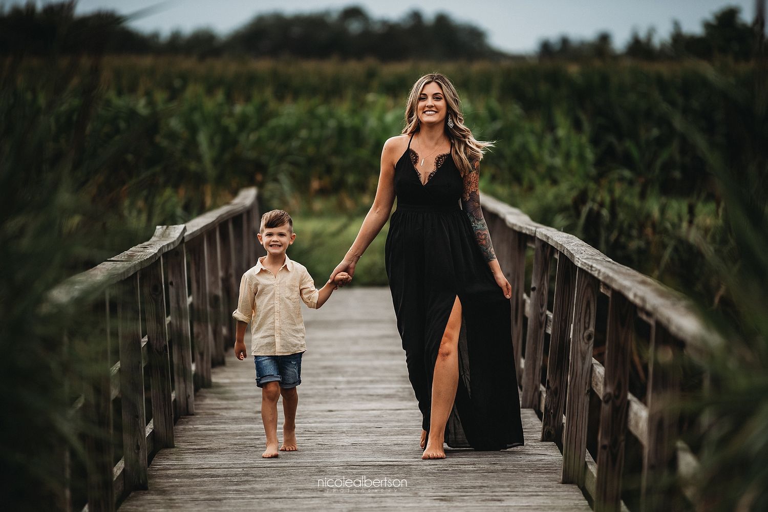 Mother and child walking together on wooden boardwalk at sunset.