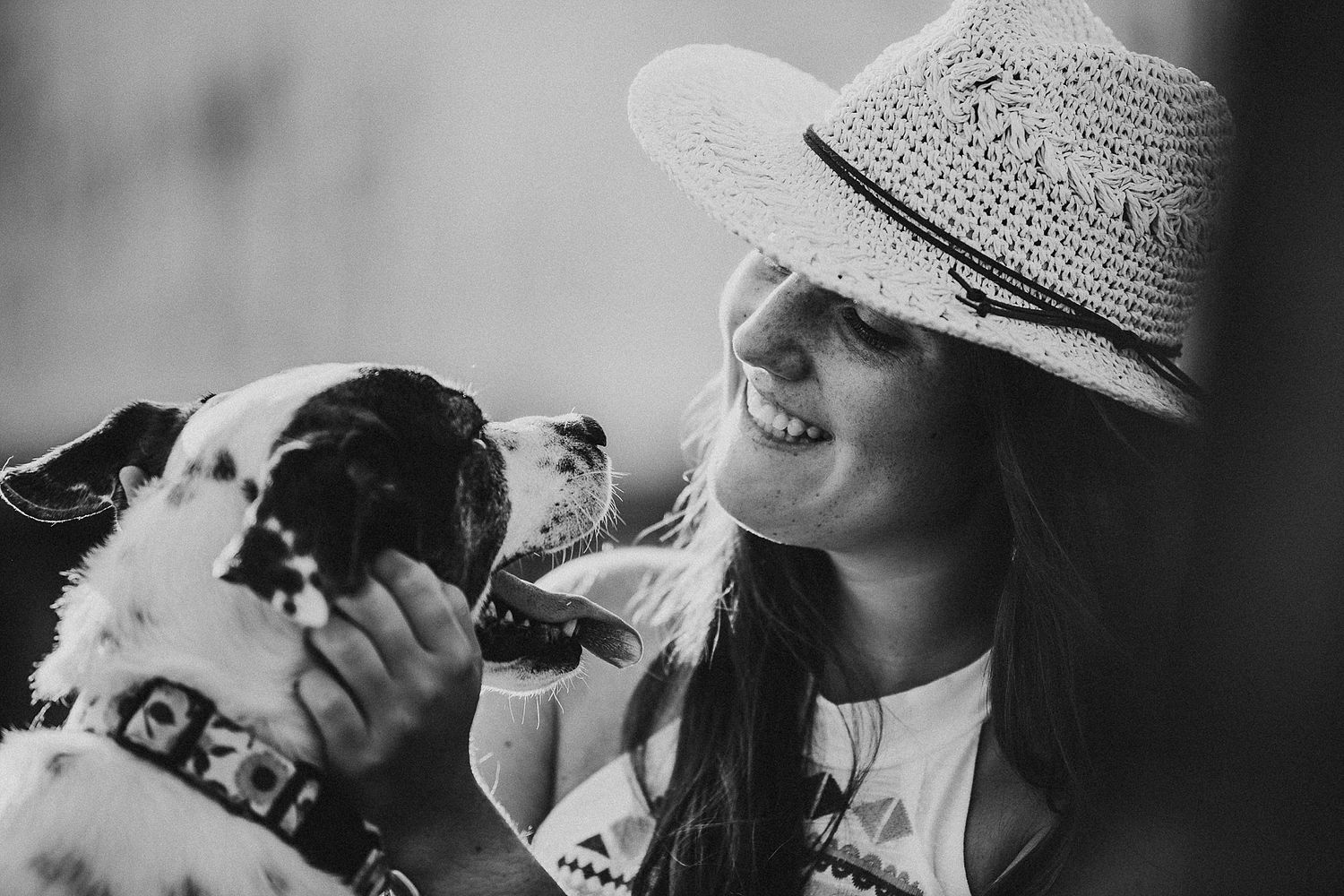 A sweet black and white dog shares an affectionate moment with someone wearing a straw hat.