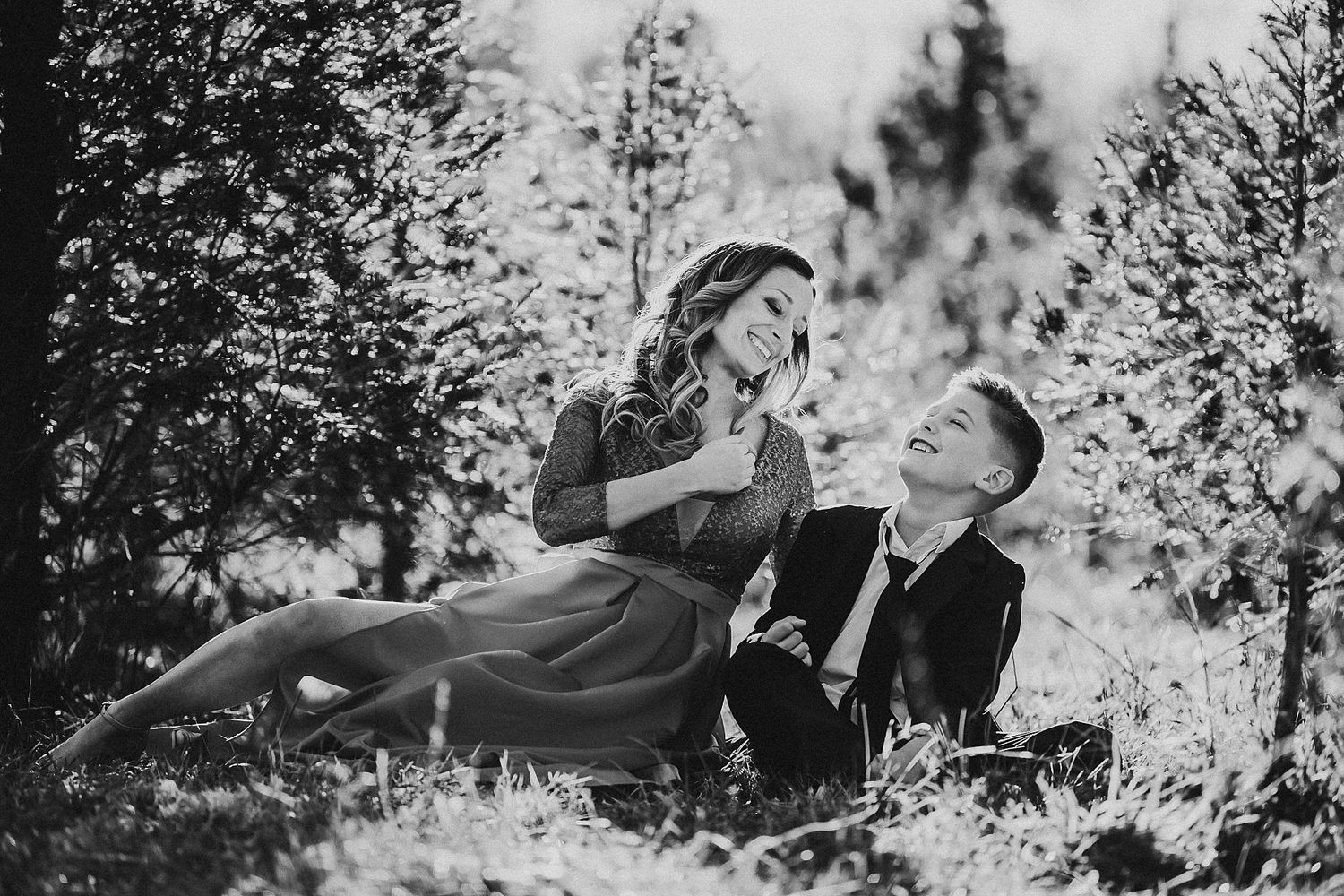 A dramatic black and white photo captures a romantic pose among pine trees.