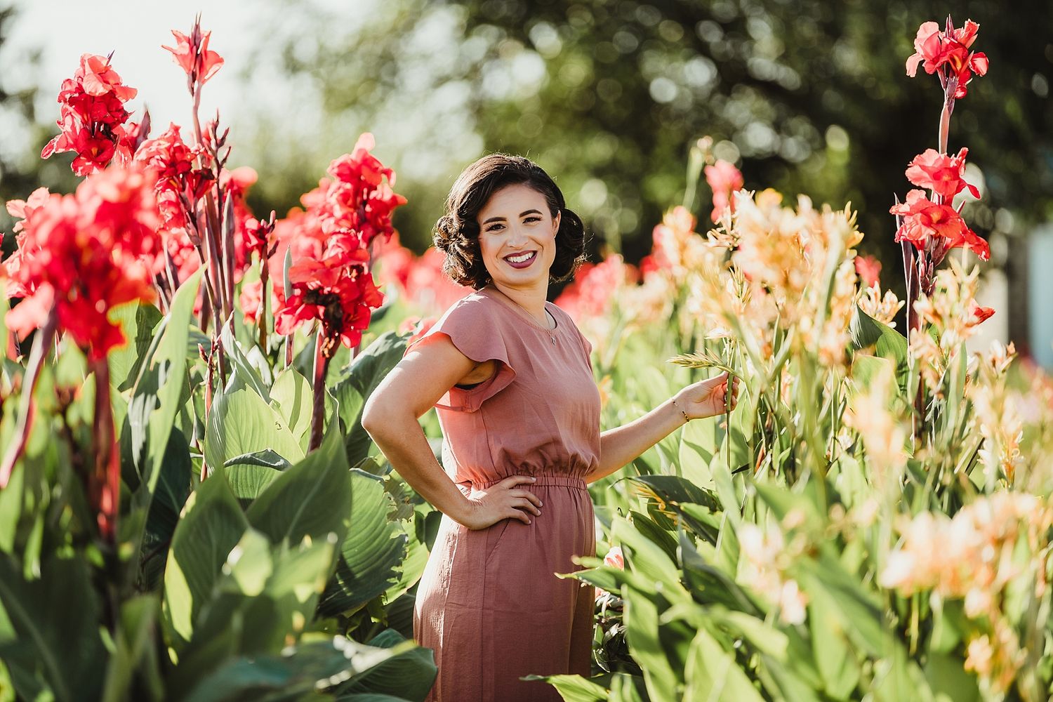 A vintage-style portrait among bright red canna lilies in a summer garden.