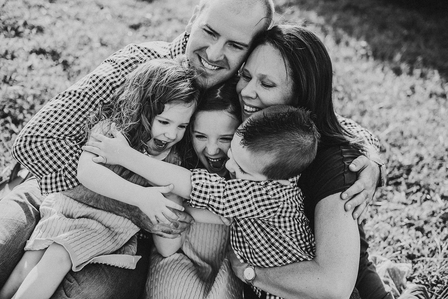 A black and white portrait captures a warm family embrace outdoors.