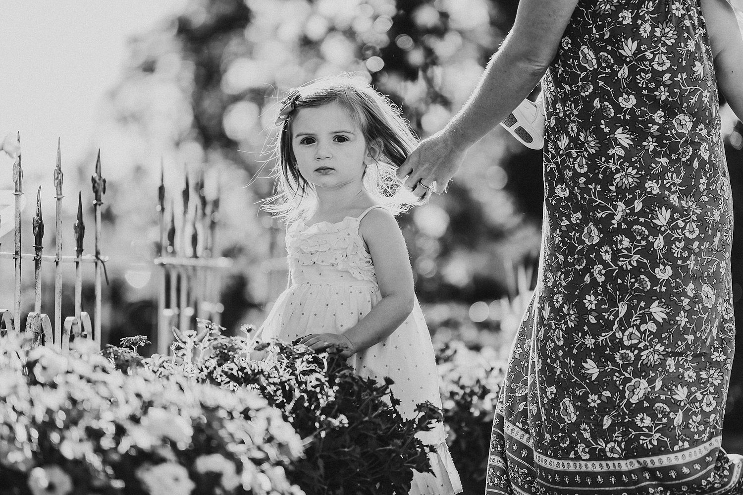 Black and white image of child in garden with floral dress and adult holding flowers.
