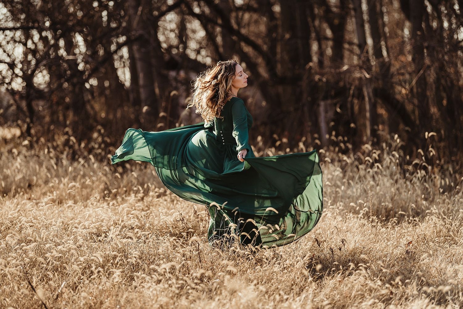 Woman in flowing emerald dress twirling in autumn field.