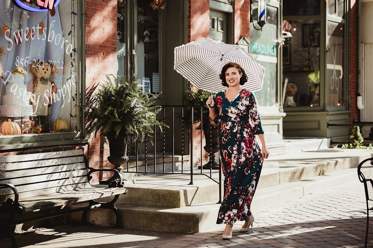 Person with parasol in floral dress walking past vintage storefronts.
