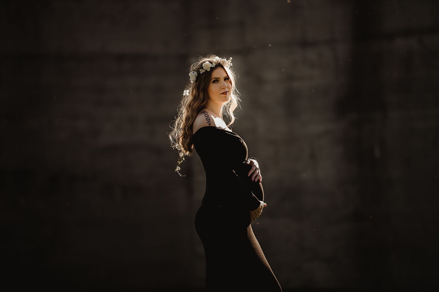 Silhouette of an expecting mother in a black dress against a dark background.