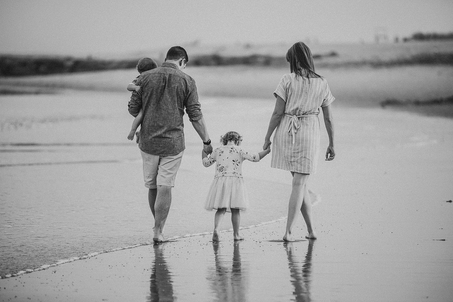 Family walking together holding hands on a beach at sunset in black and white.