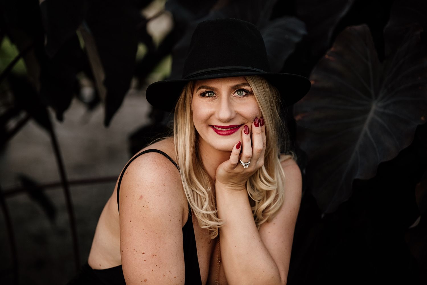 Portrait of someone in a black hat against dark foliage background.