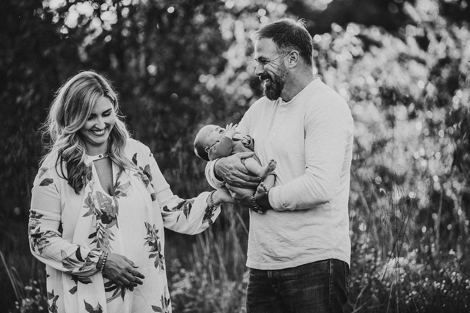 Black and white image of new parents sharing a joyful moment with their newborn outdoors.