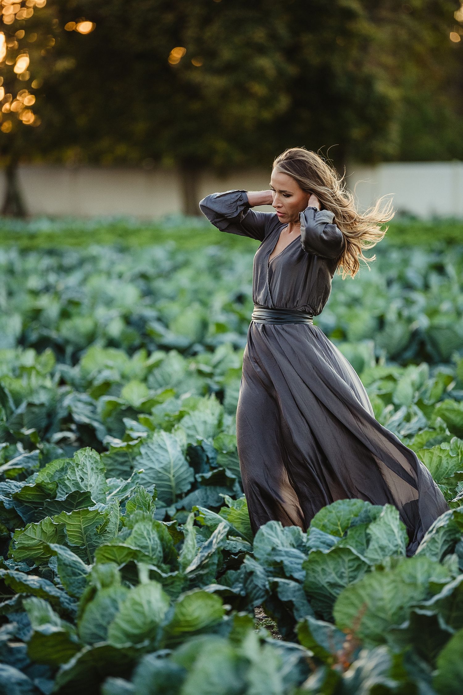 Woman in flowing gray dress twirls in a cabbage field during golden hour.