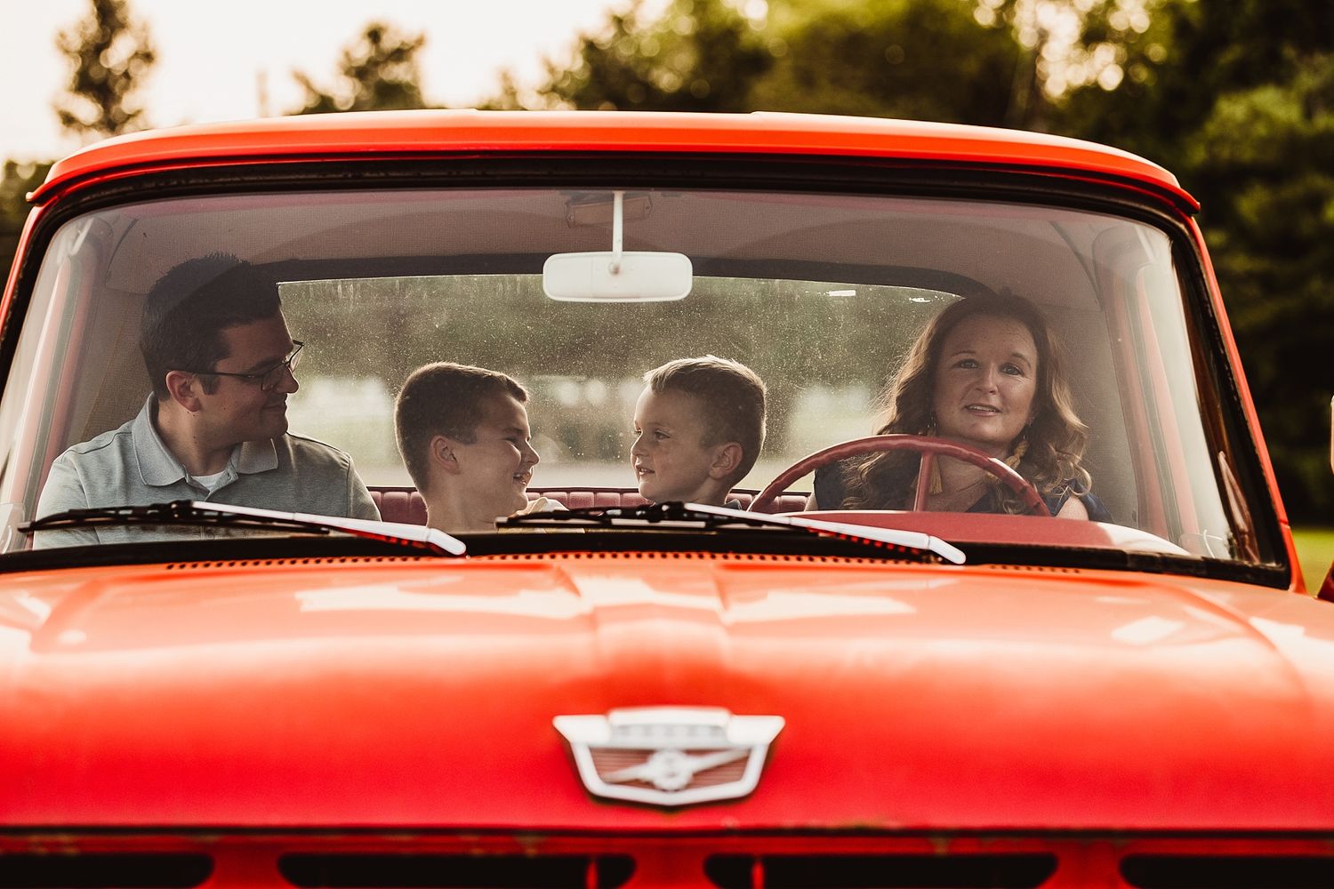 A classic red car filled with passengers smiling and enjoying a drive together on a sunny day.