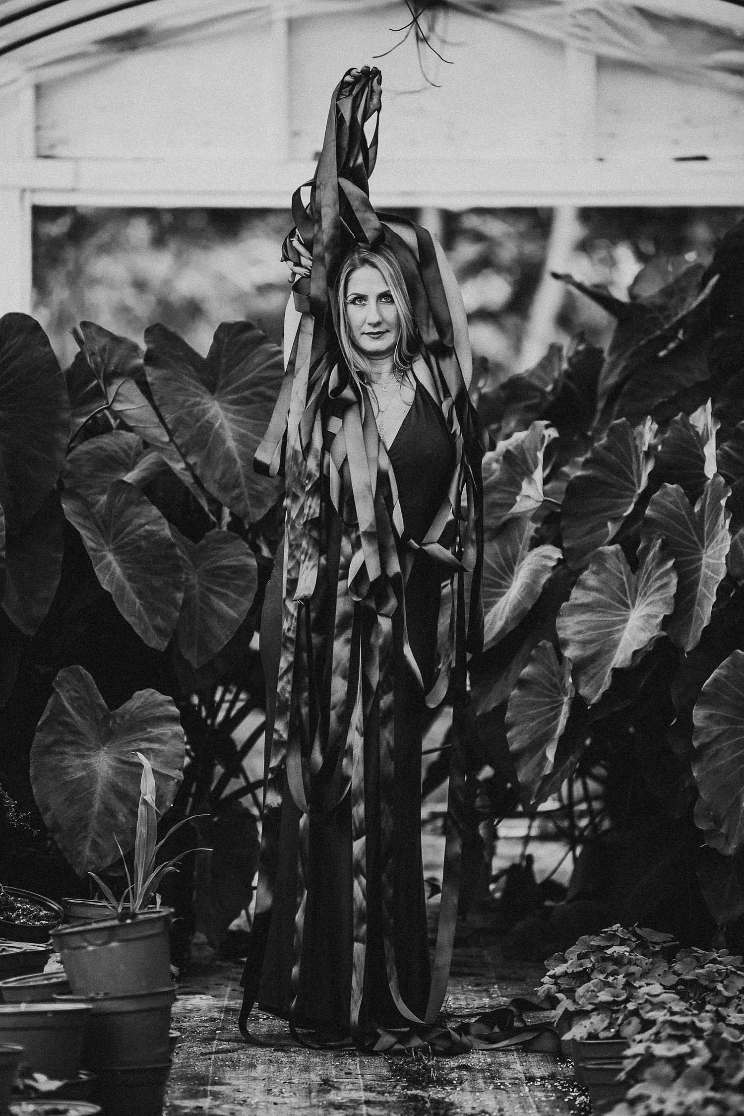 A dramatic black and white portrait among large tropical leaves in a greenhouse setting.
