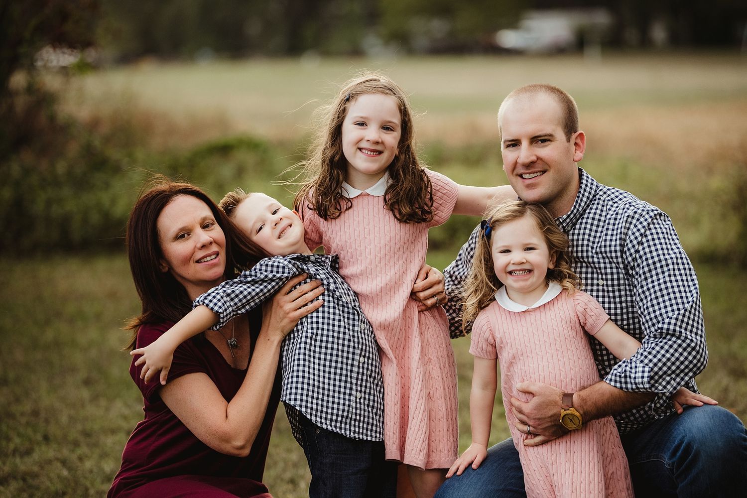 Happy family laughs together outdoors wearing coordinated outfits in burgundy, pink and gingham.