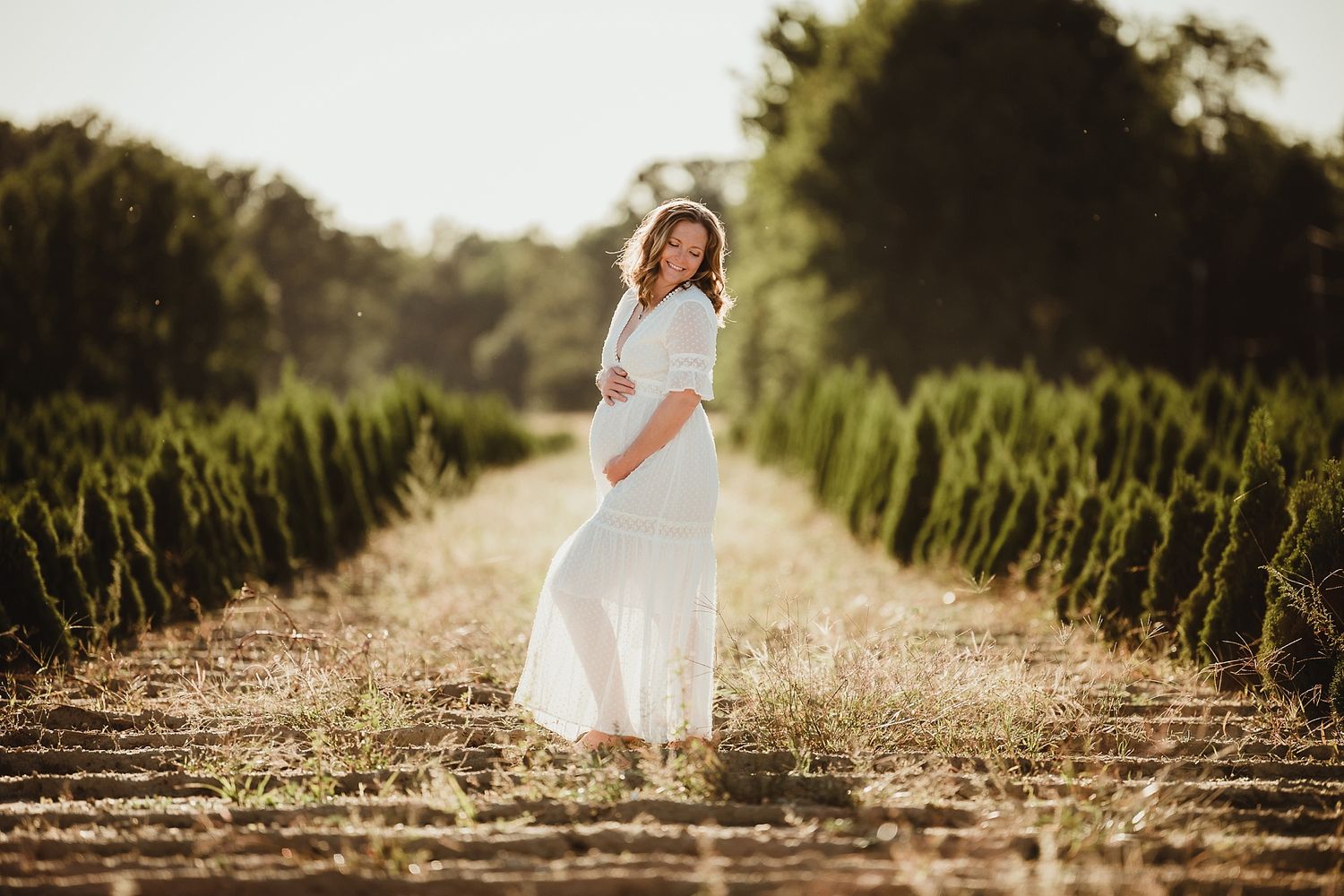 Woman in white dress poses elegantly in vineyard at golden hour.
