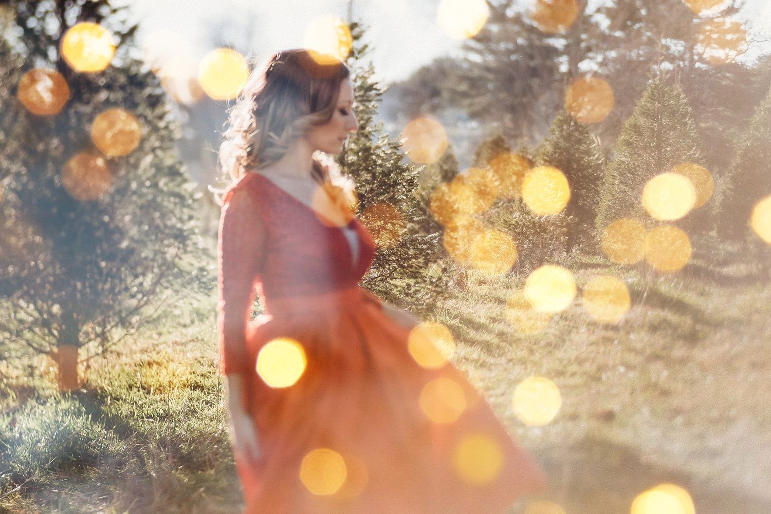 Dreamy portrait with bokeh lights of woman in red dress at sunset.