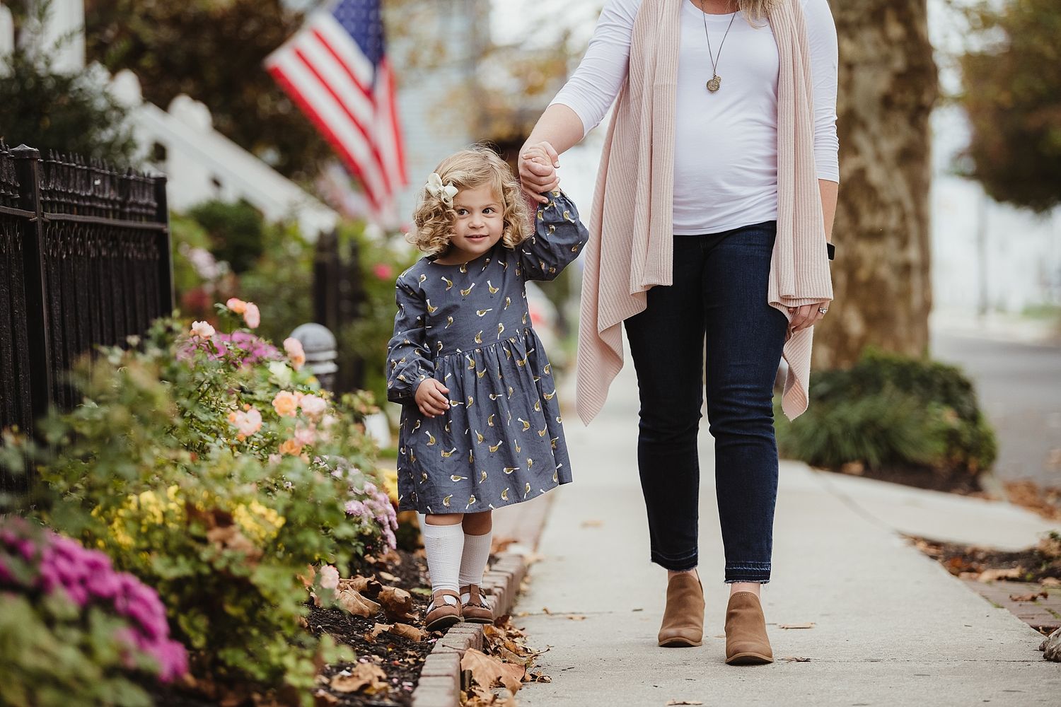 Walk along autumn sidewalk with American flag and pink flowers in background.
