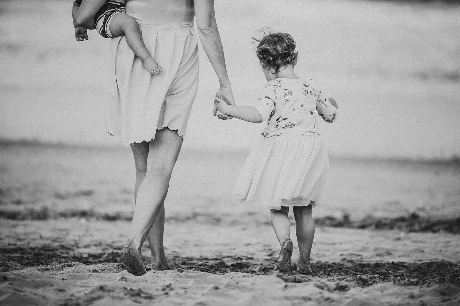 Black and white image of legs walking together on sandy beach.