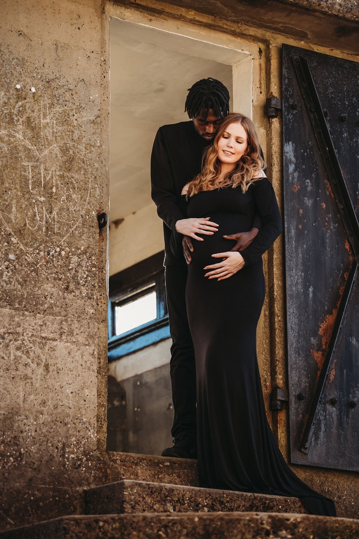 Romantic maternity photo of couple in black attire posed in rustic doorway.