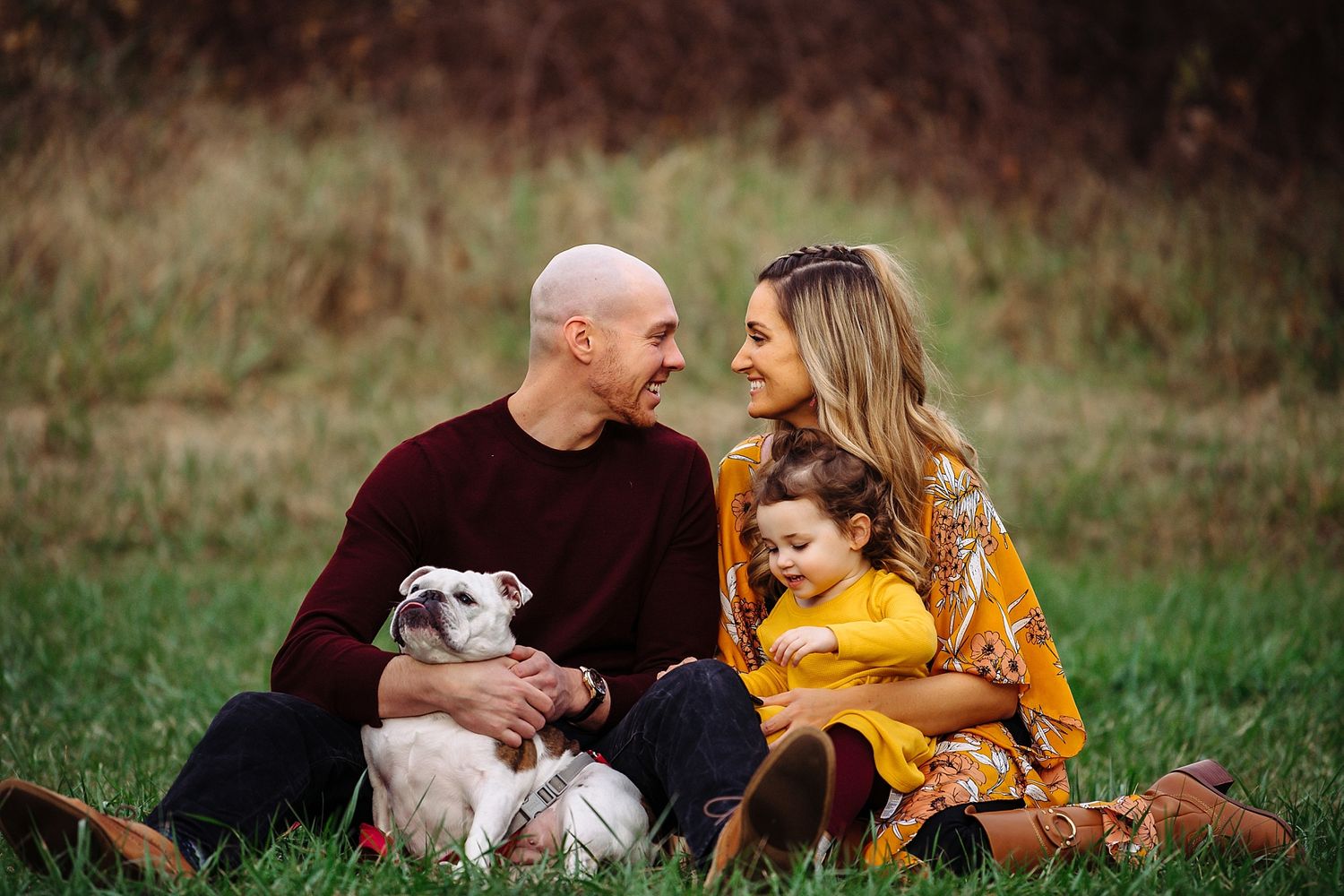 Family and their small dog sitting together in a grassy field during an outdoor photo session.