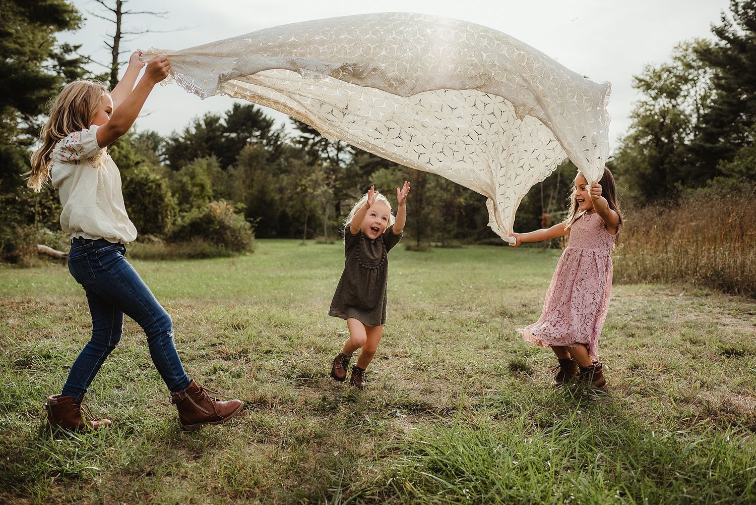 Three people playing with white lace fabric outdoors on a sunny day.