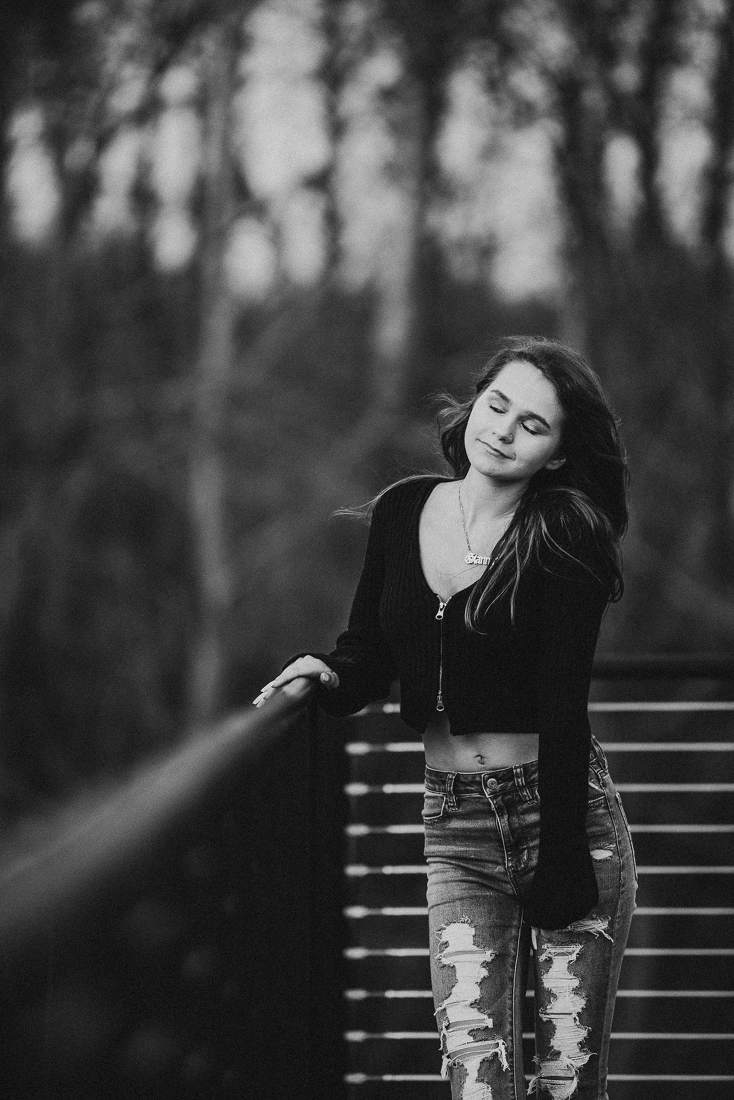 Black and white portrait of person leaning on railing in moody forest setting.