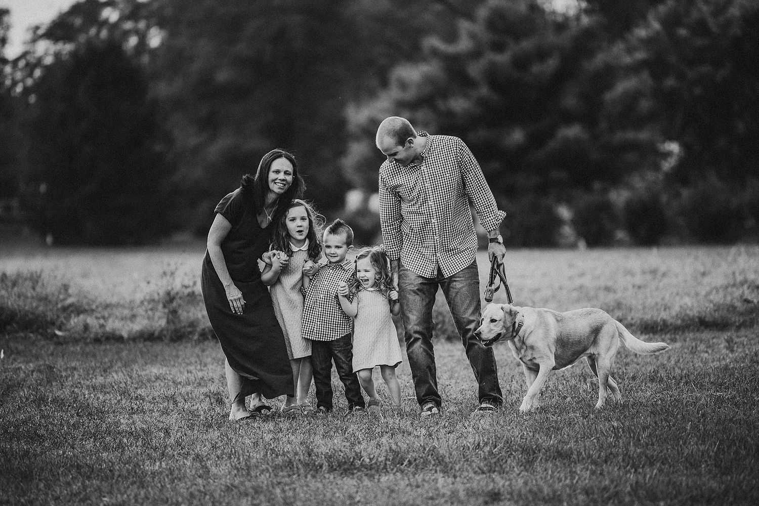 Black and white family portrait with dog in grassy field.