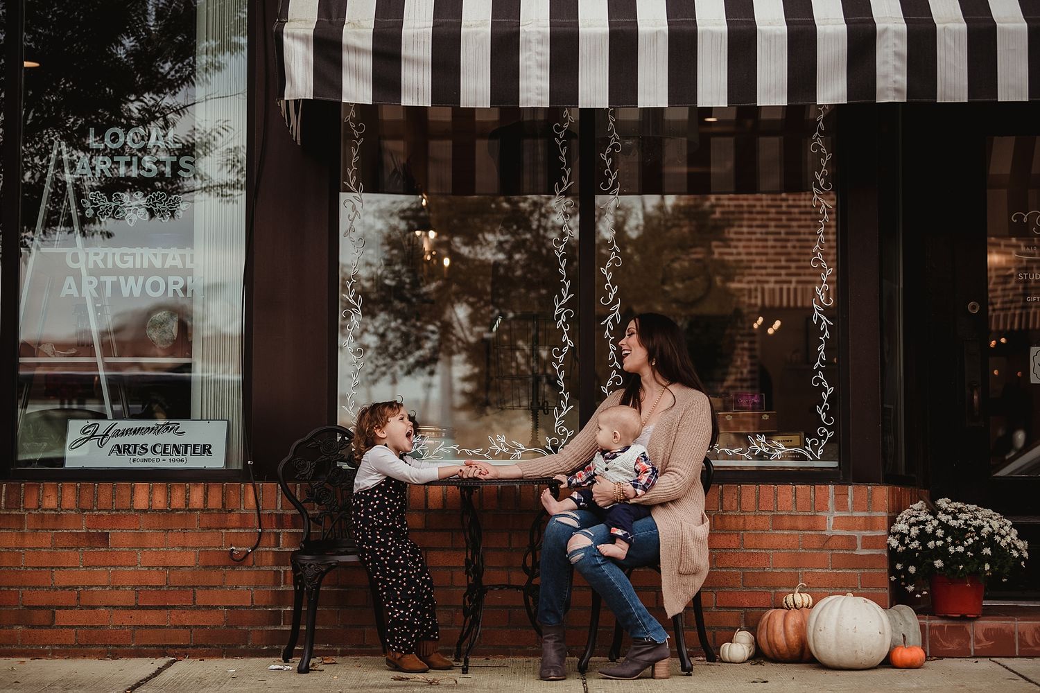 A cozy autumn scene outside a storefront with striped awning and decorative pumpkins.