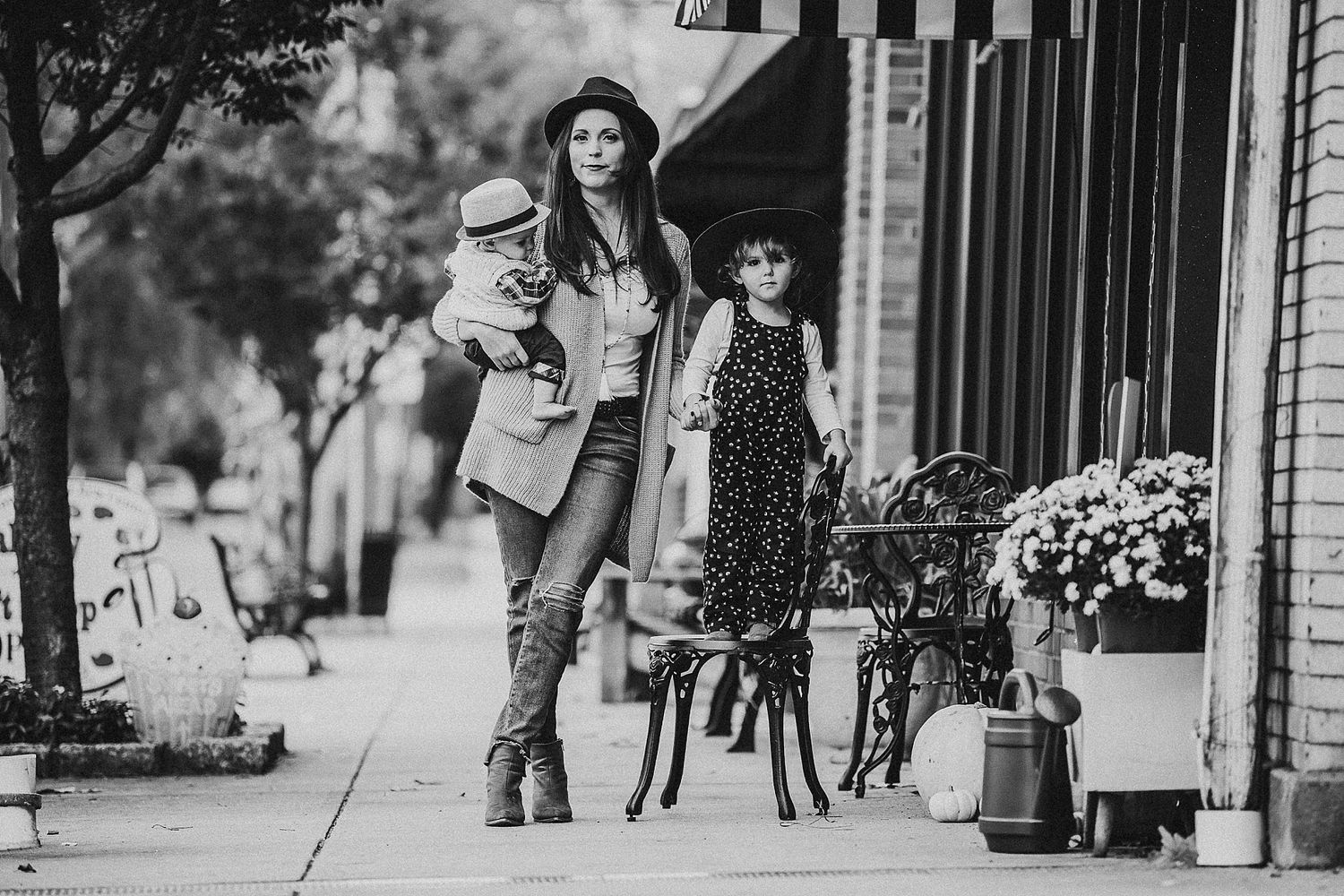 A black and white street scene with flowers and storefronts on a city sidewalk.