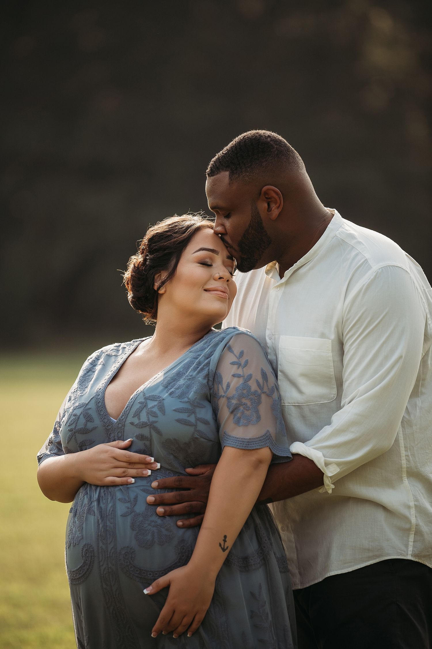 A tender moment between an expectant couple in a sunlit field.