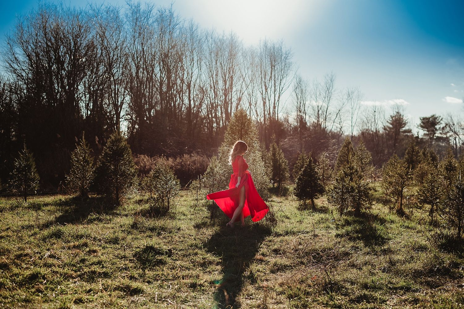 Person in red dress twirls through winter field at sunset with bare trees in background.