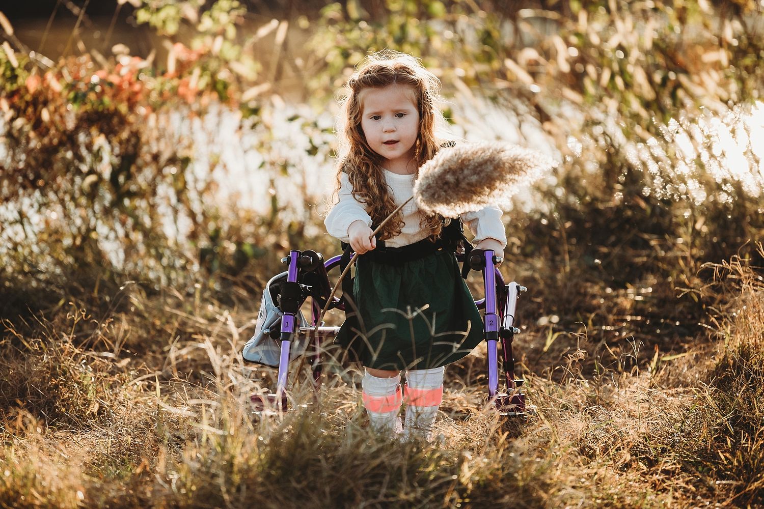 Young child in dress holding gifts outdoors in golden sunlight.