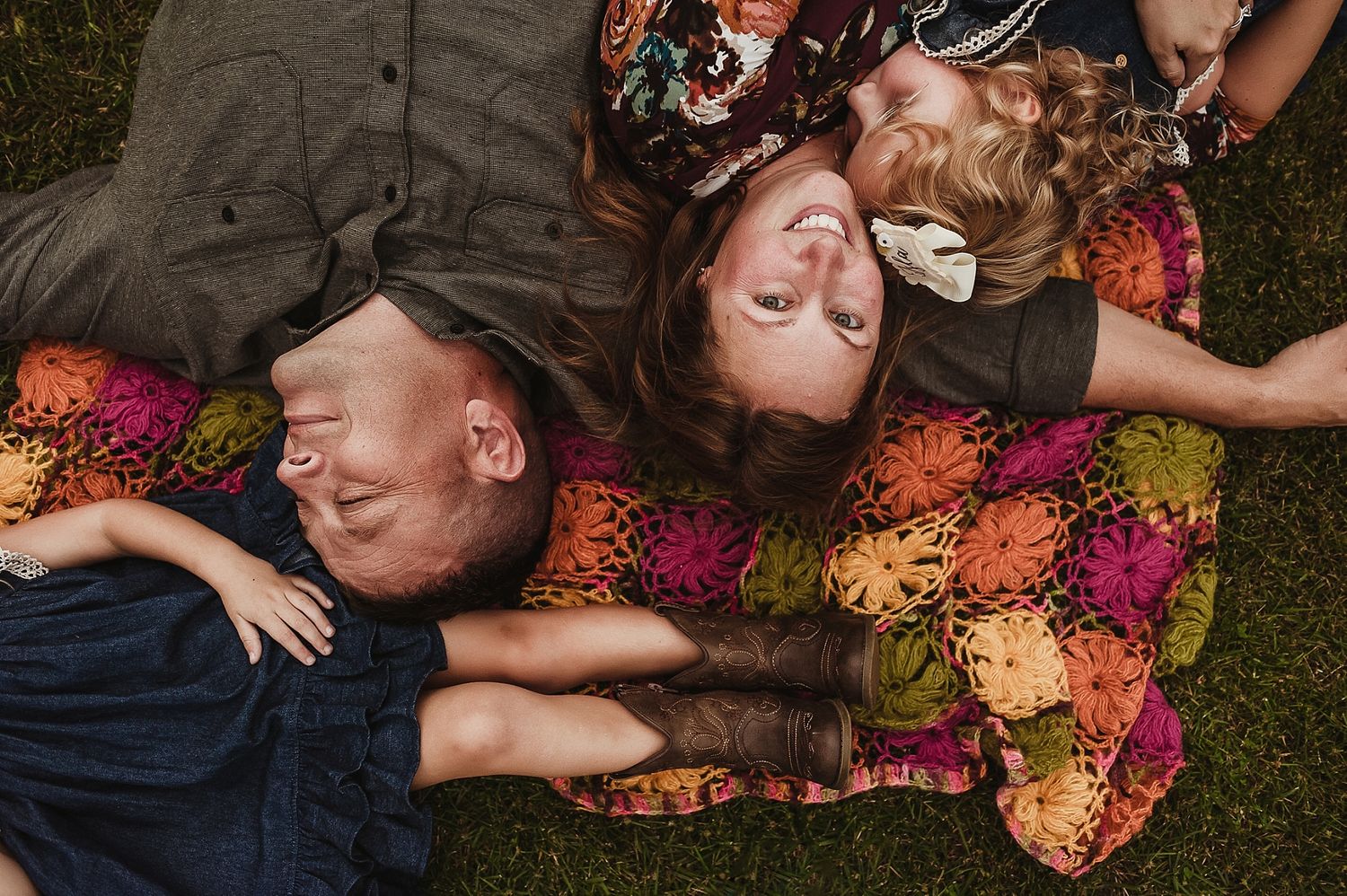 Overhead view of family lying on colorful blanket in grass during golden hour.