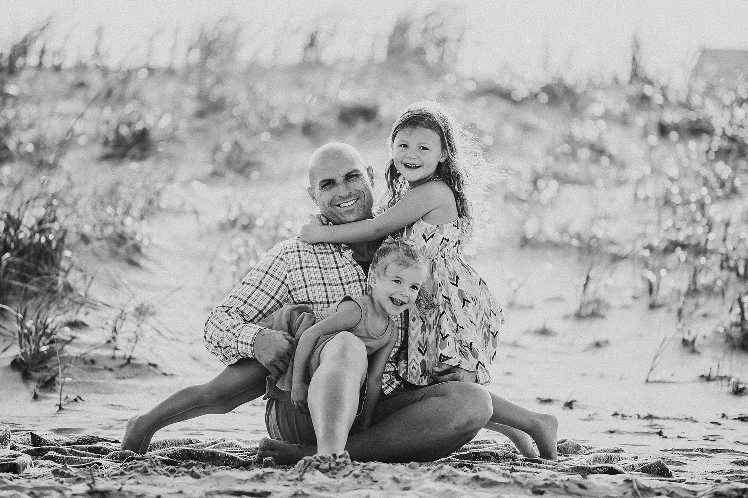 Black and white beach portrait showing playful family moment in sand dunes.