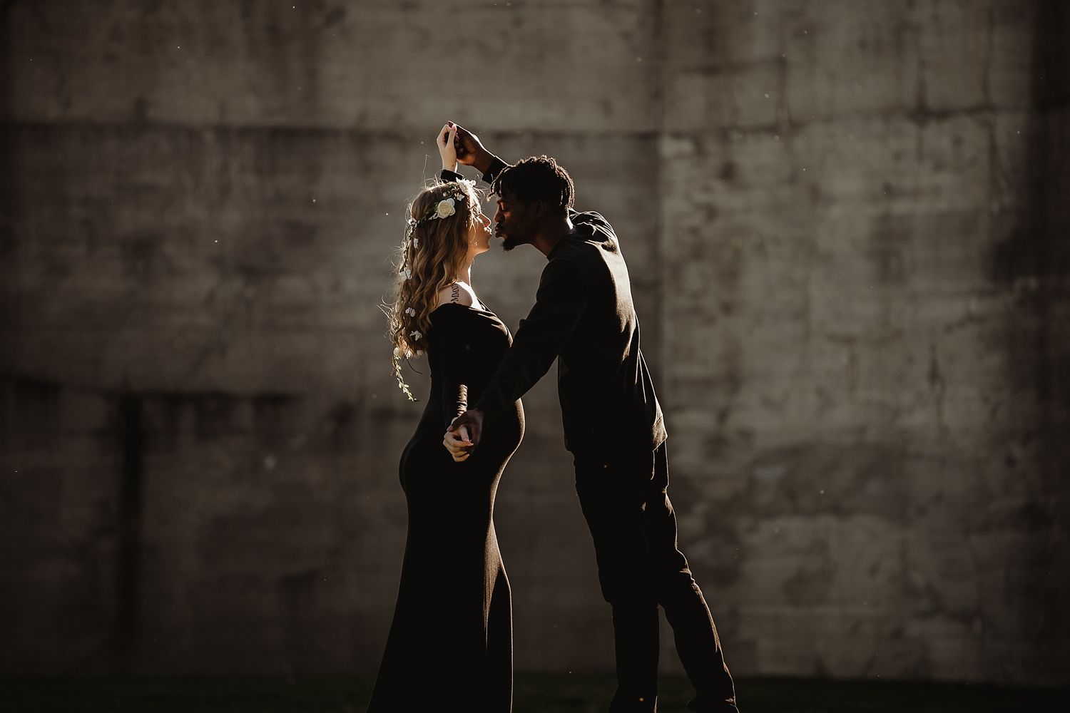 Dramatic dance pose silhouetted against concrete wall in moody lighting.