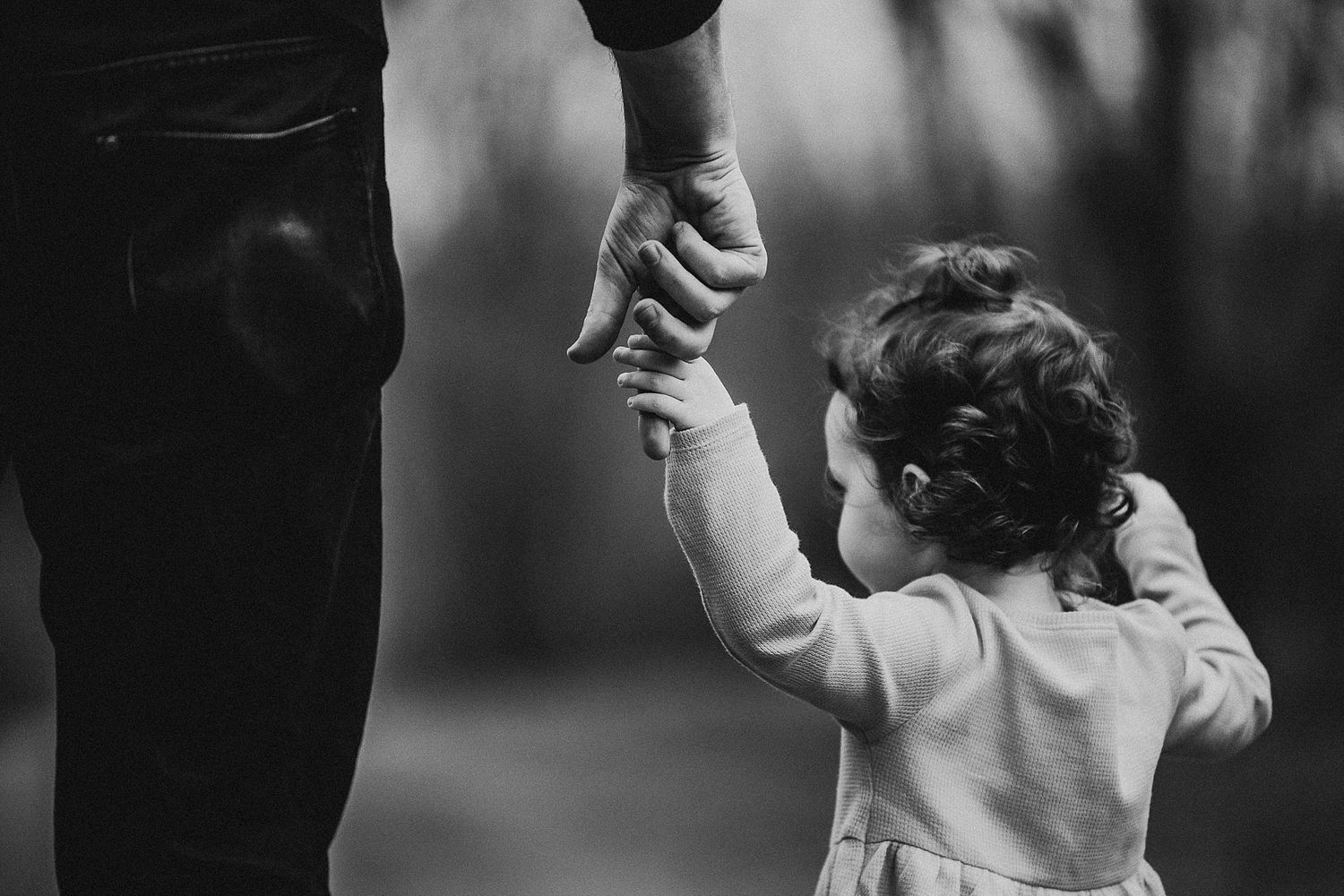 Black and white image of small hand reaching up to hold adult hand.