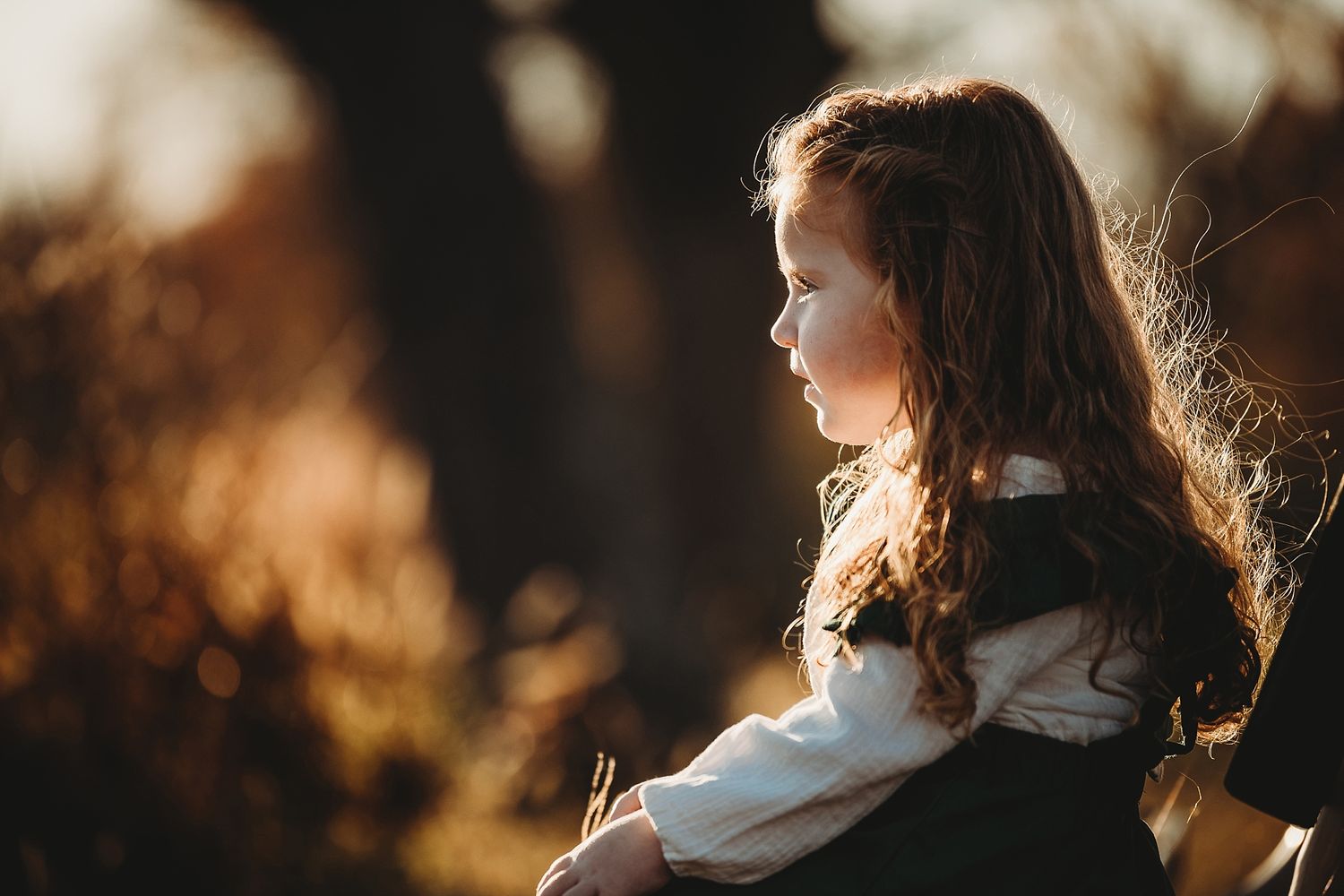 Side profile of a young person with long hair illuminated by golden sunlight in nature.
