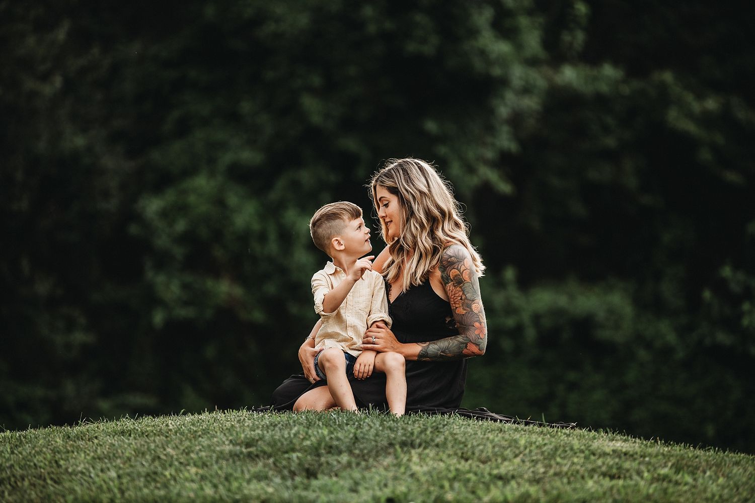 Candid moment of mother and child sitting together on grassy hillside in warm sunlight.