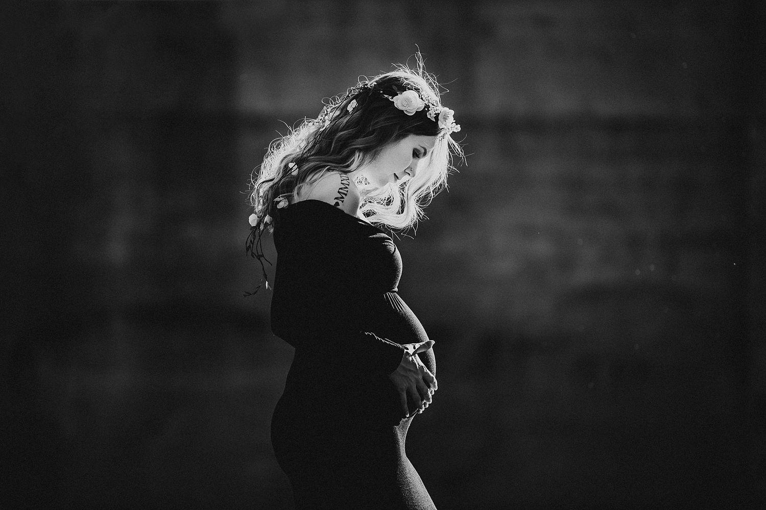 Black and white artistic portrait of person in dark clothing with flowing hair against moody background.