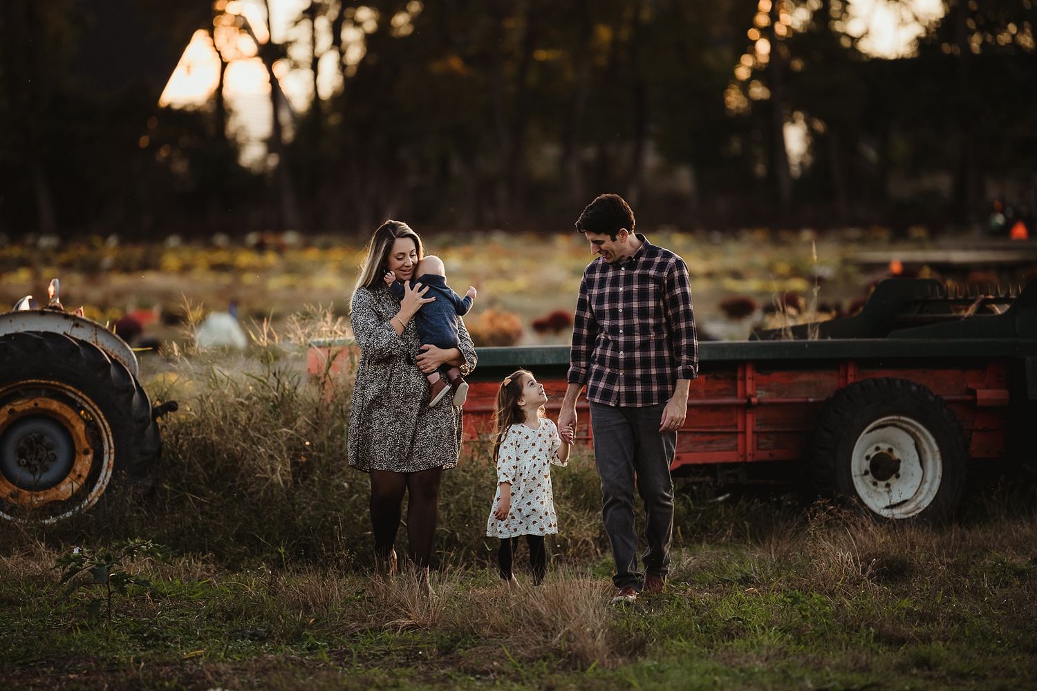 Family standing together in rustic setting with vintage tractor during golden hour.