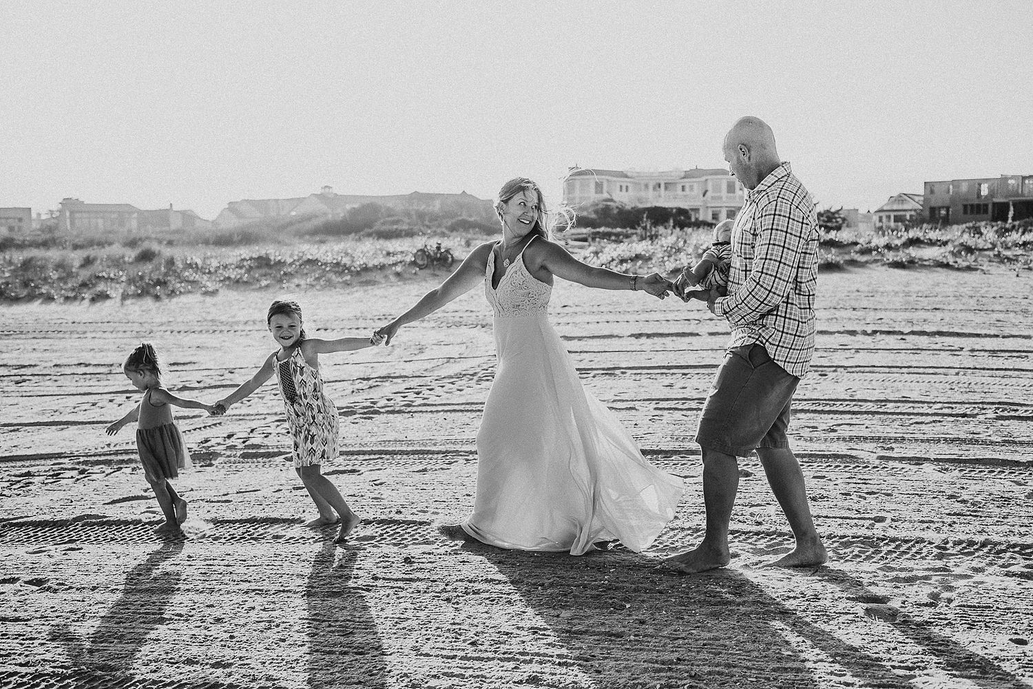 Black and white photo of family holding hands and dancing together on beach.