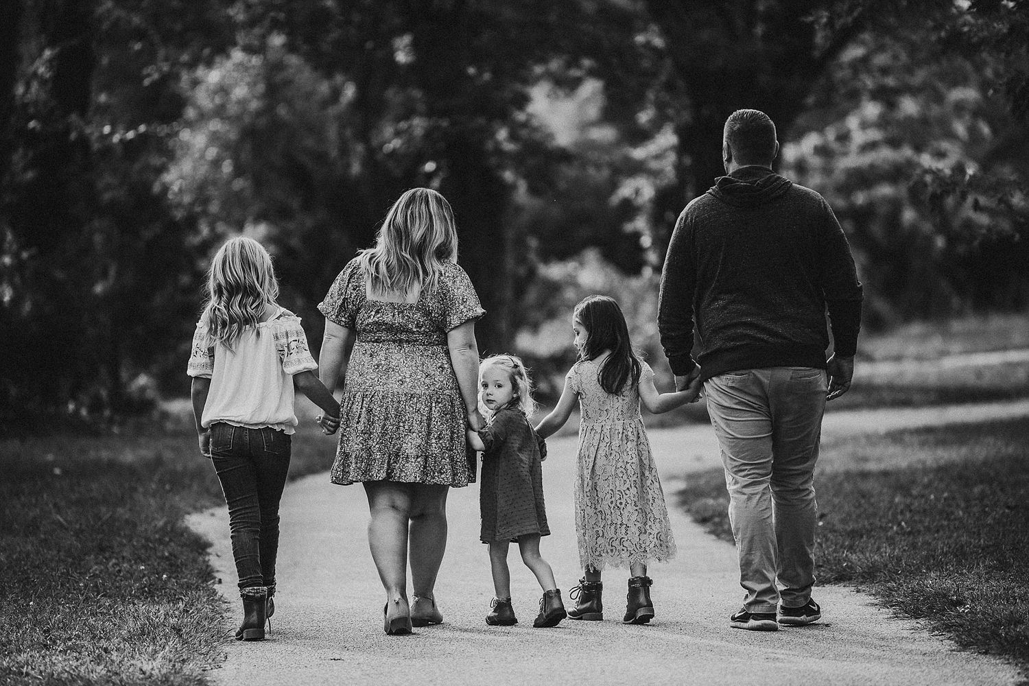 A family walks together on a tree-lined path in black and white.
