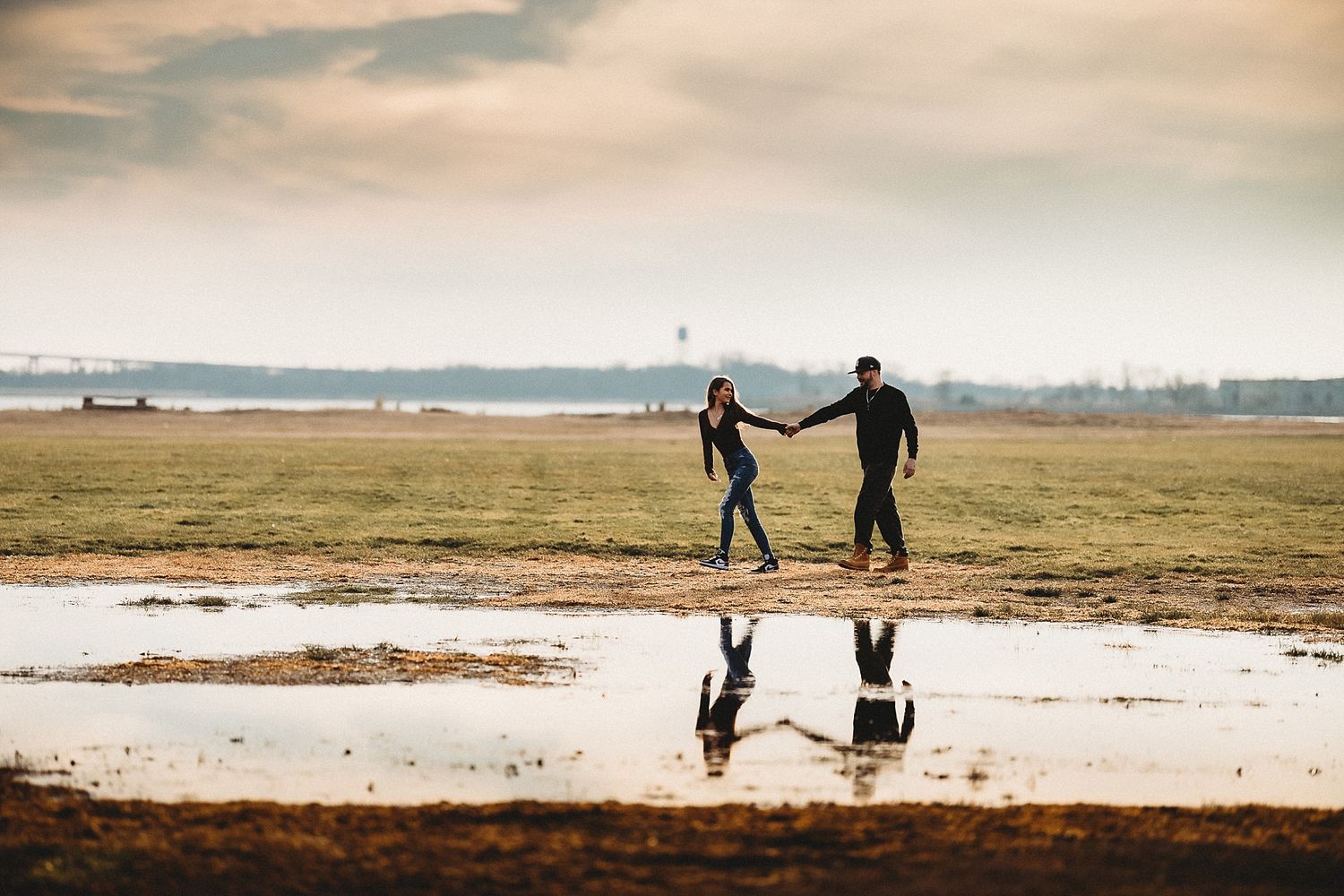 Two people walking on a beach with their reflection mirrored in the wet sand beneath dramatic clouds.