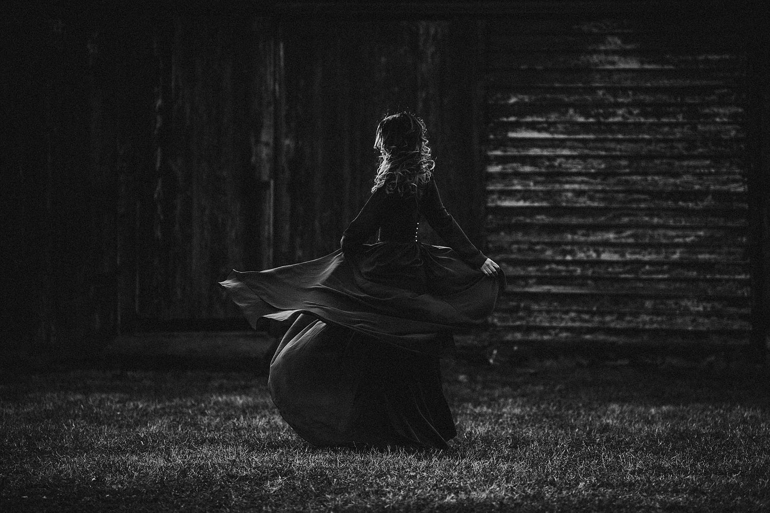 A silhouetted figure spins in a flowing dress against a dark wooden backdrop.