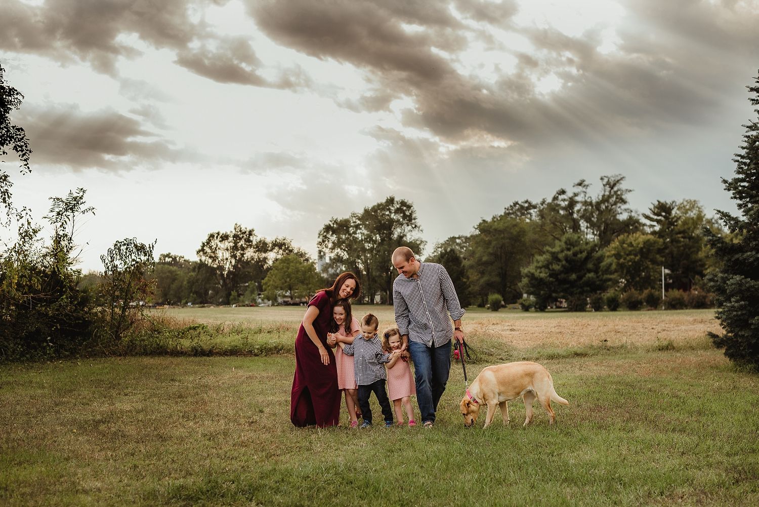 A family and their dog pose together in a golden field at sunset.