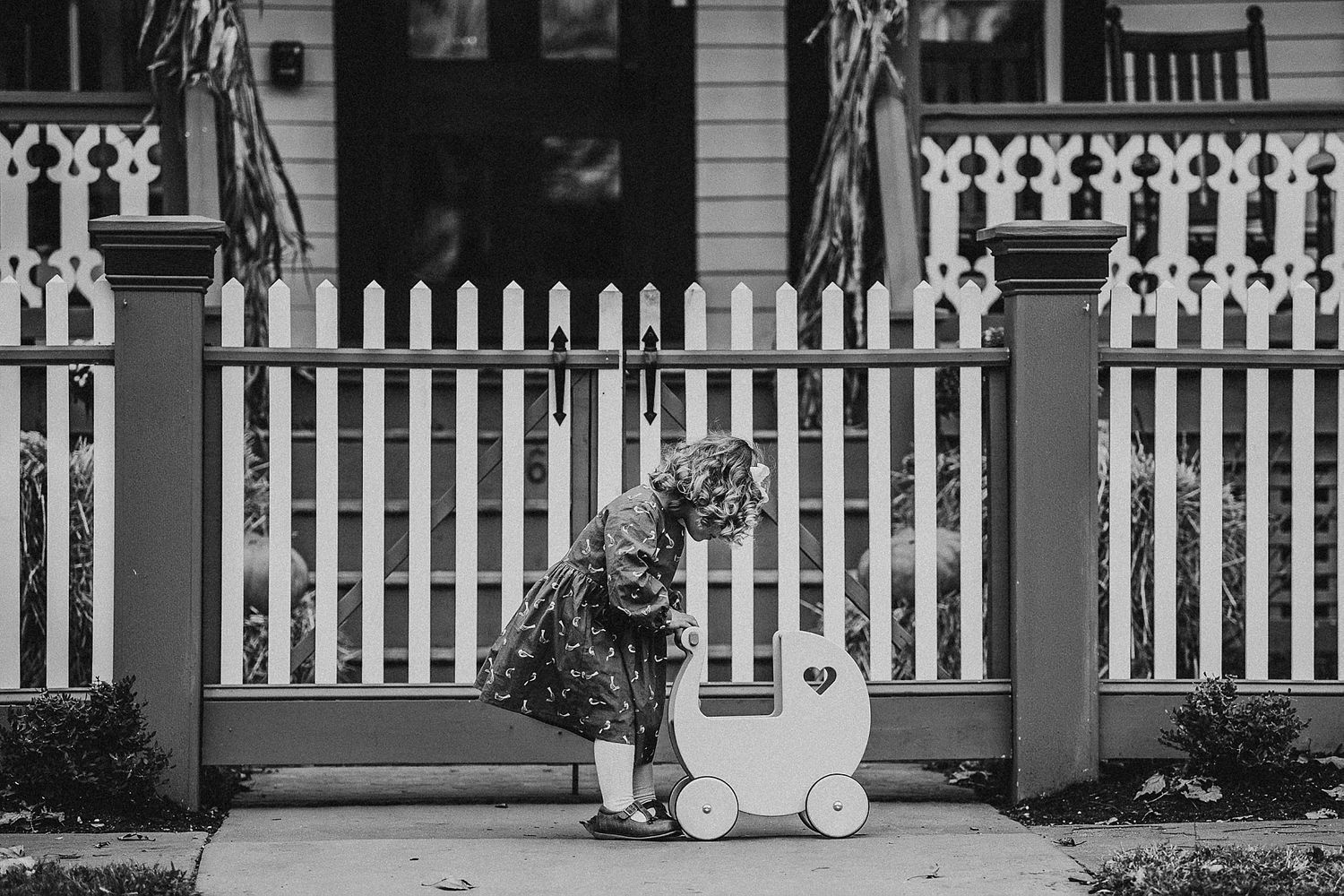 A small child plays with a toy cart behind a white picket fence.