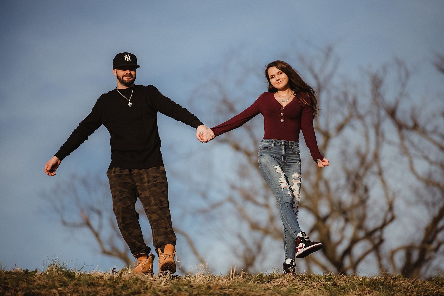 Two people hold hands while balancing on a hilltop against a moody sky.