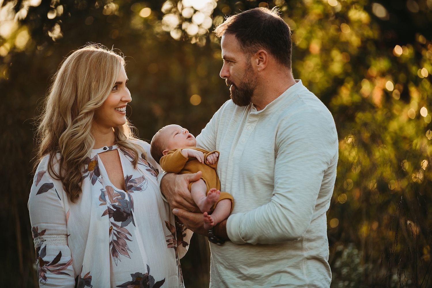 A couple shares a tender moment with their newborn baby in golden sunset light.