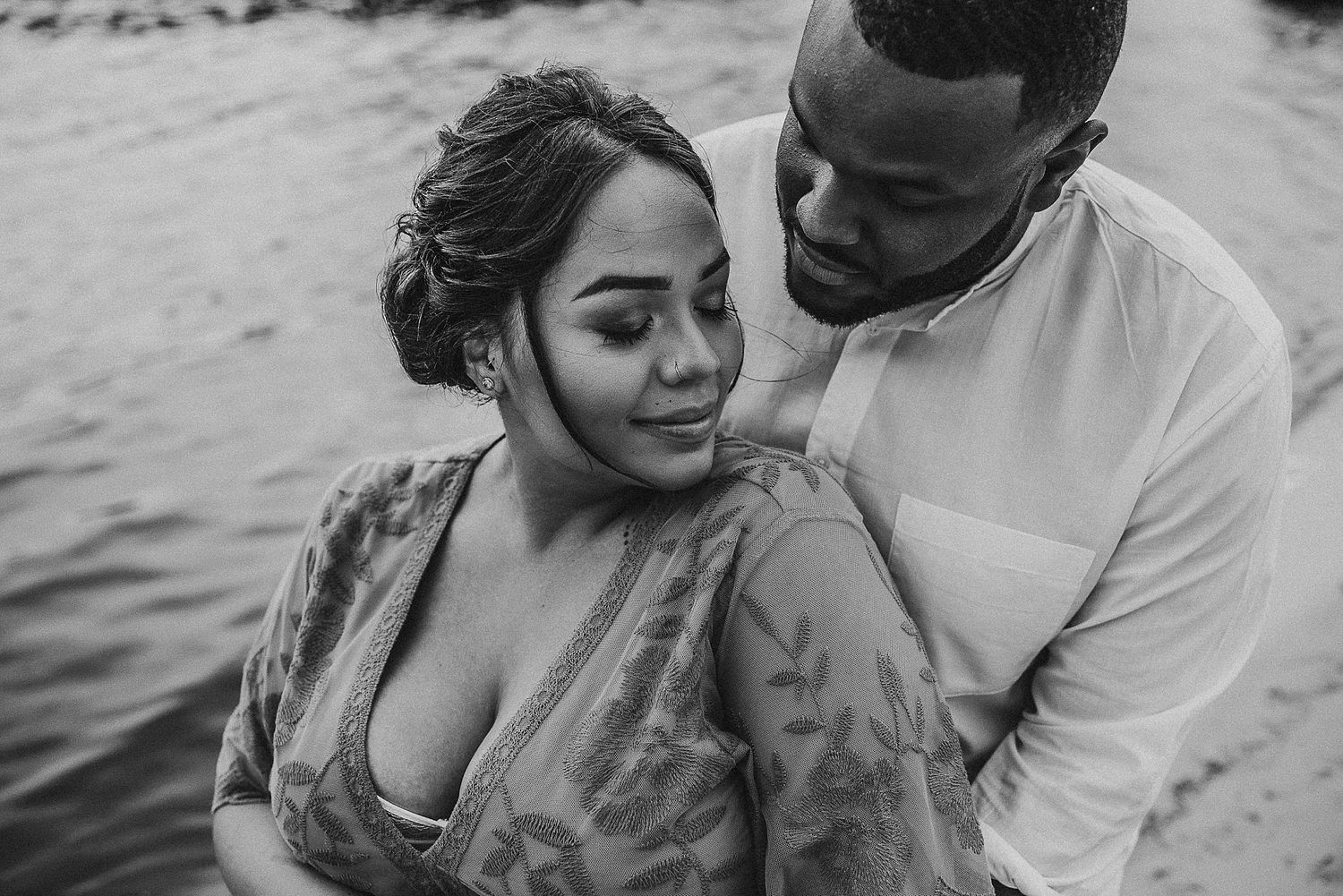 Intimate couple embracing by the water in a romantic black and white portrait.