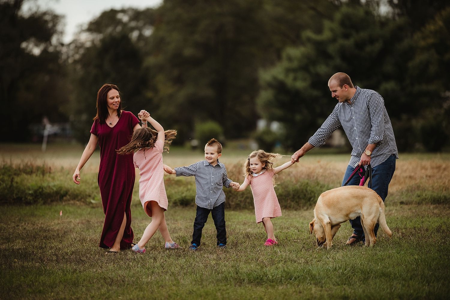Family playing in a field with children and their golden retriever during golden hour.