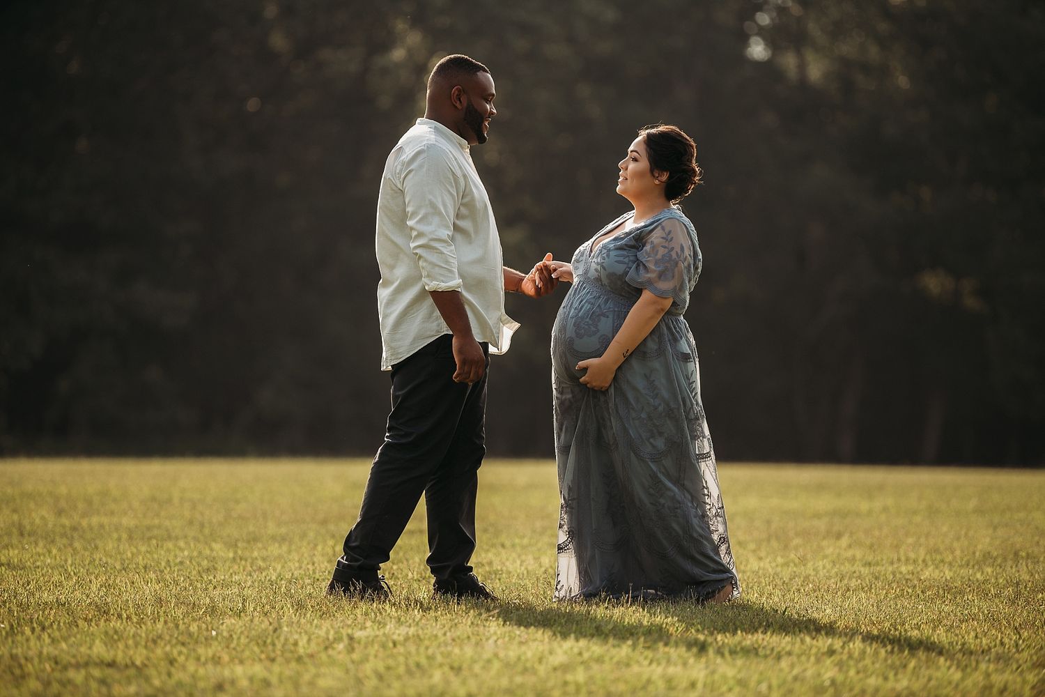 Expectant couple sharing a tender moment together in a sunny field.