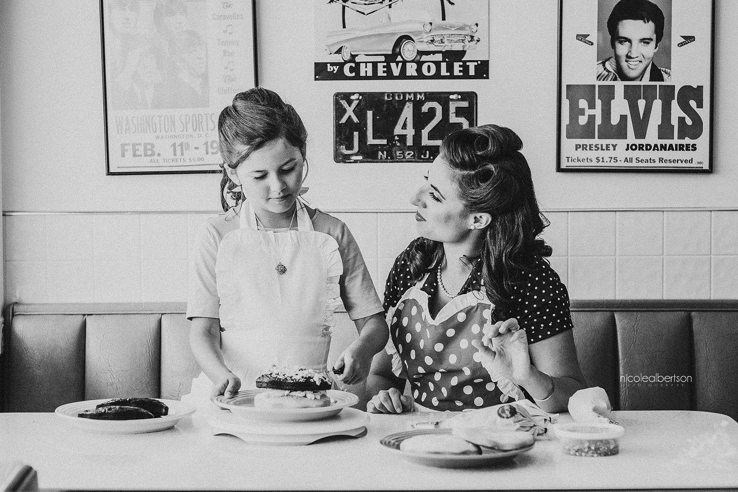 Black and white photo of retro diner scene with vintage Elvis poster on wall.